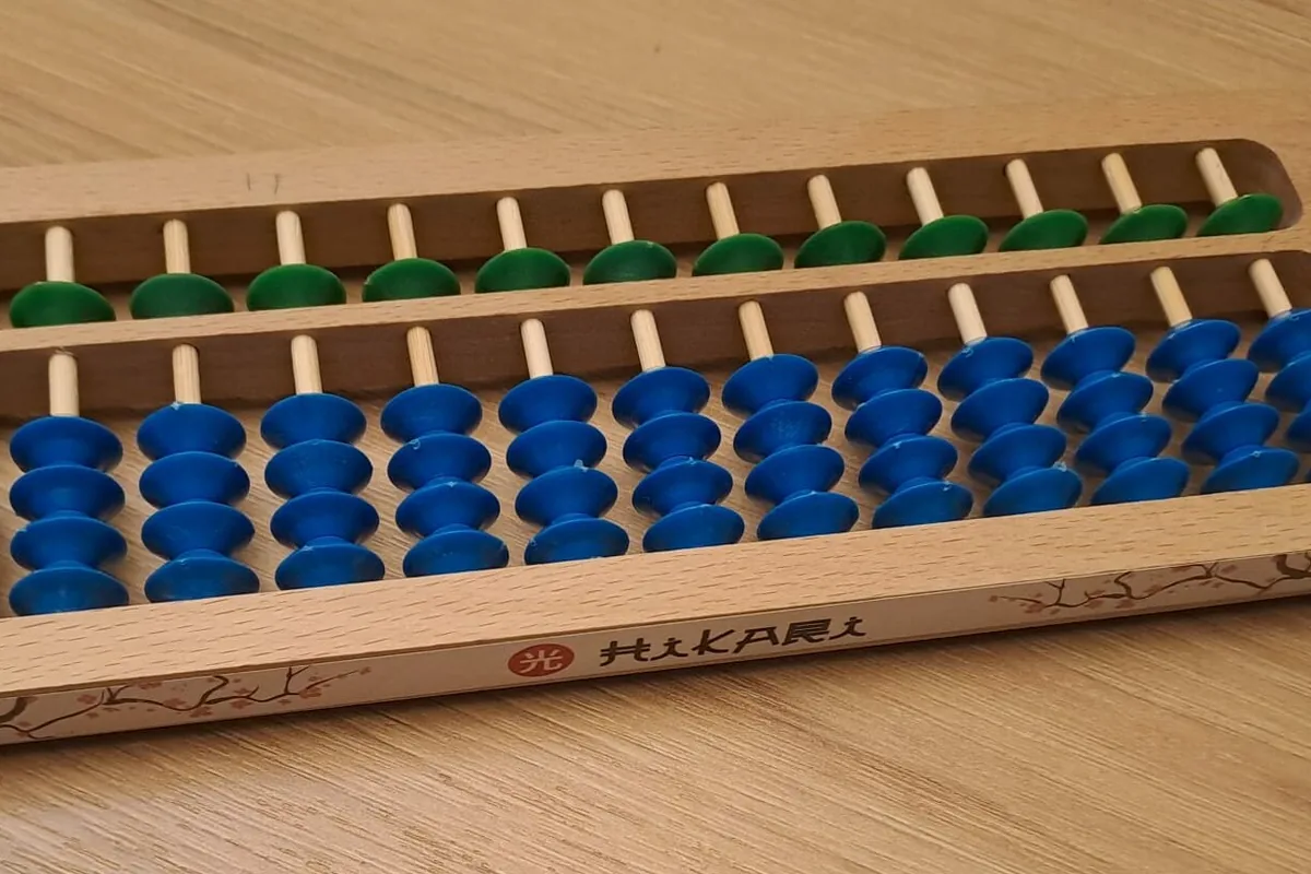 Ein Soroban-Abakus mit grünen und blauen Perlen auf einem Holztisch