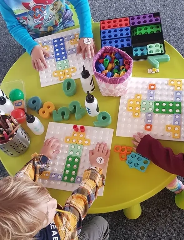 Kinderhände legen bunte Numicon-Formen auf Steckplatten, von oben auf den gelben Tisch gesehen